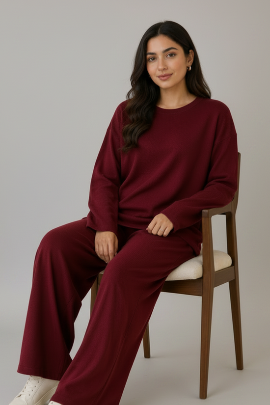 Woman sitting on a chair wearing a burgundy outfit with white sneakers in a bright room.