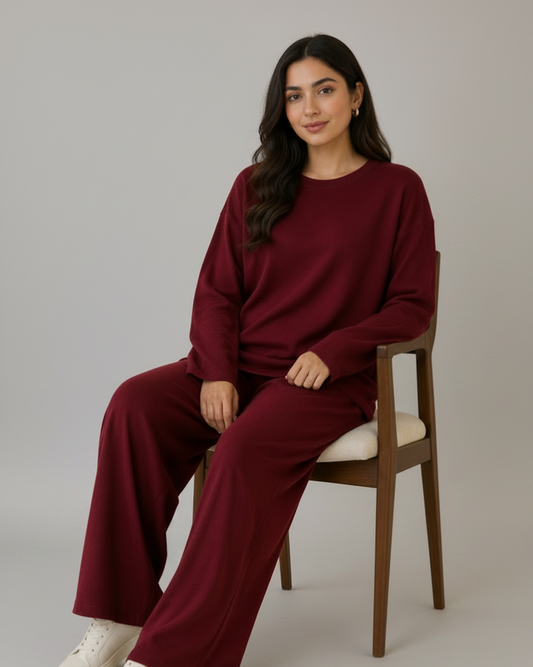 Woman sitting on a chair wearing a burgundy outfit with white sneakers in a bright room.