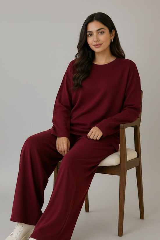 Woman wearing a Chillpjs burgundy longline top and wide-leg trousers co-ord set, sitting on a wooden chair.