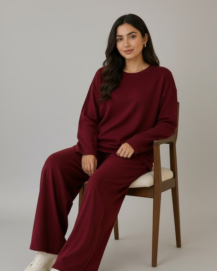Woman wearing a Chillpjs burgundy longline top and wide-leg trousers co-ord set, sitting on a wooden chair.