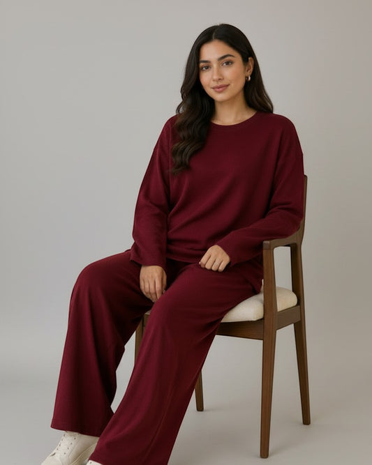 Woman wearing a Chillpjs burgundy longline top and wide-leg trousers co-ord set, sitting on a wooden chair.