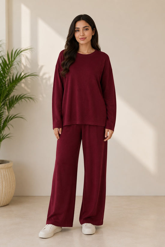 Woman wearing a Chillpjs burgundy longline top and wide-leg trousers co-ord set in a minimalist indoor setting.
