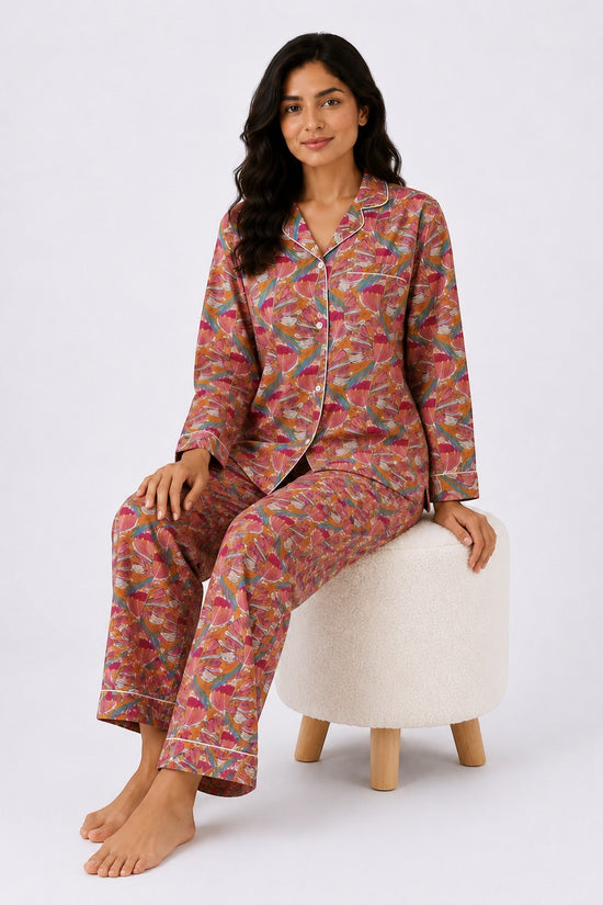 A woman wearing a Chillpjs floral linen night set with coral, pink, and teal print, button-down top, and trousers.