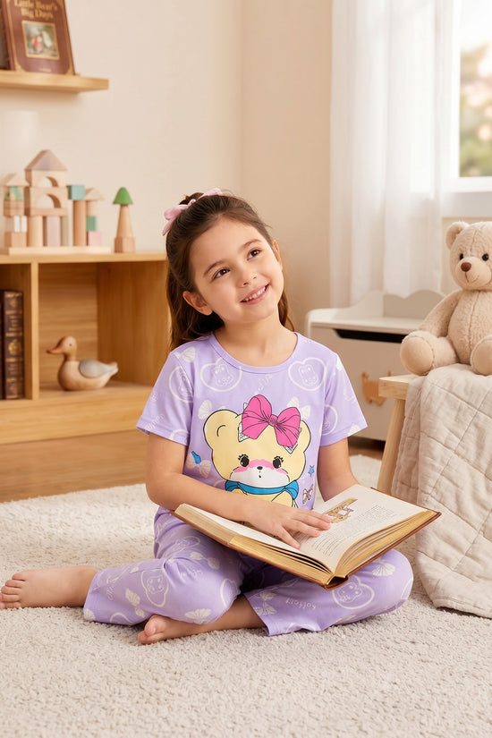 Chillpjs lavender cotton night suit with a cute teddy bear print worn by a young girl reading a book on a rug.