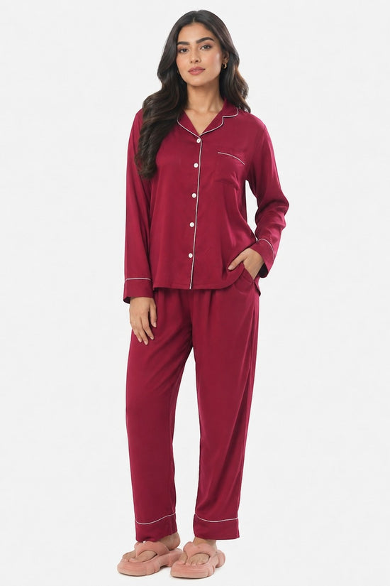 Model wearing a maroon Chillpjs satin silk pajama set with white piping, long sleeves, and matching pants.