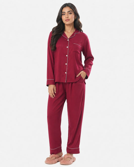 Model wearing a maroon Chillpjs satin silk pajama set with white piping, long sleeves, and matching pants.