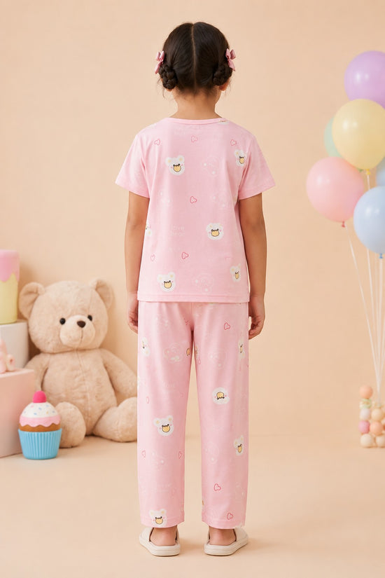 Chillpjs pink cotton night suit with bear and cupcake print worn by a young girl, back view in a cozy room.