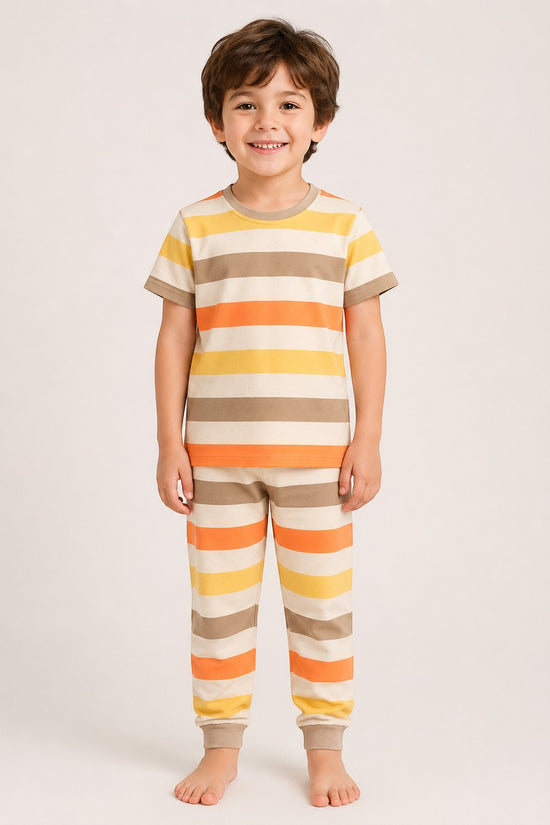 A smiling boy wearing a Chillpjs cotton pajama set with retro sunset-colored horizontal stripes and ribbed trim.