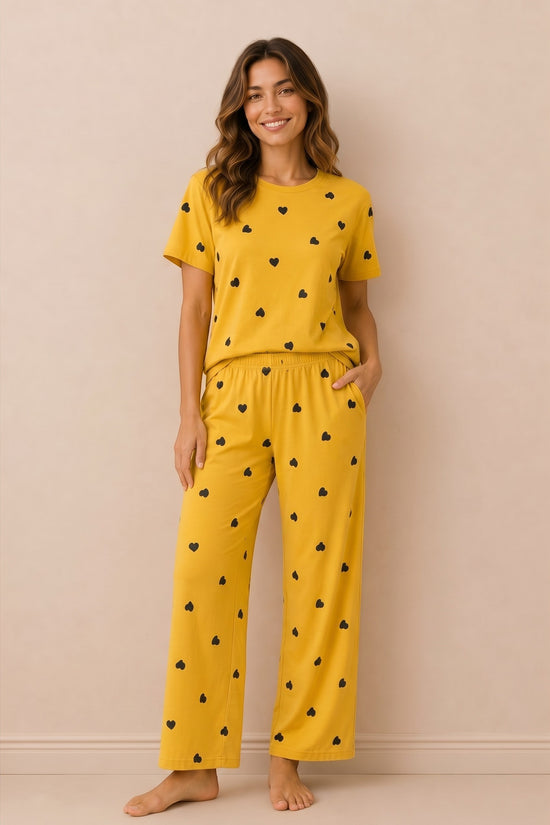 Model wearing Chillpjs marigold yellow pajama set with black heart print, featuring crew neck top and lounge pants.