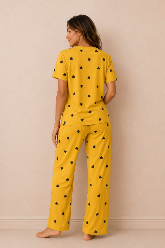 Model wearing Chillpjs marigold yellow pajama set with black heart print, featuring short sleeves and long trousers.